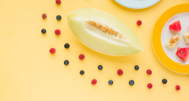 Free photo an elevated view of muskmelon decorated with blueberries and raspberries on yellow backdrop