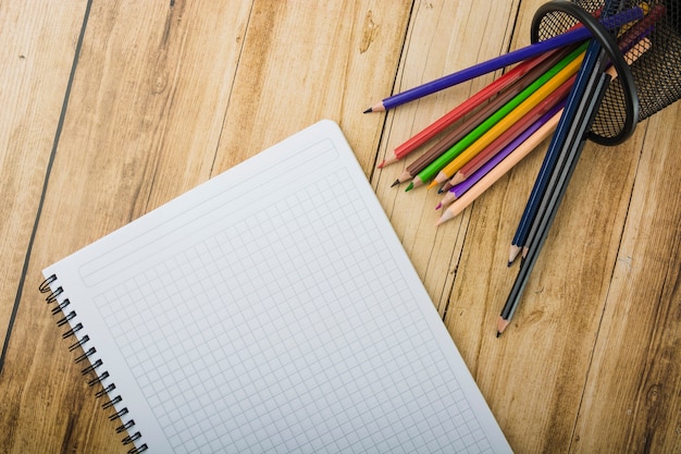 Elevated view of notepad and colorful pencils on wooden background