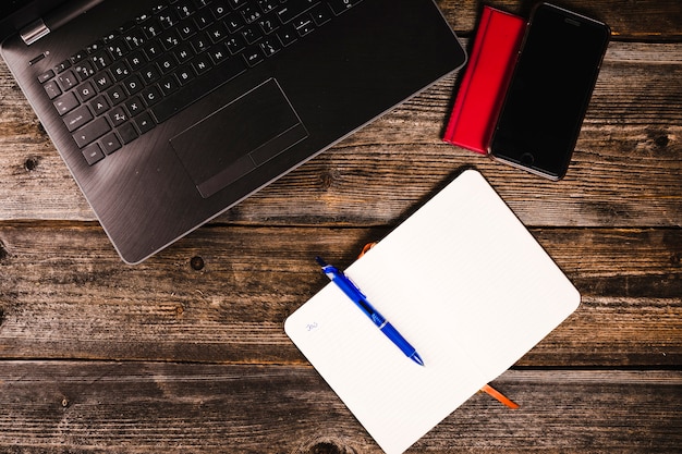 Elevated view of notepad, pen, laptop and smartphone on wooden background