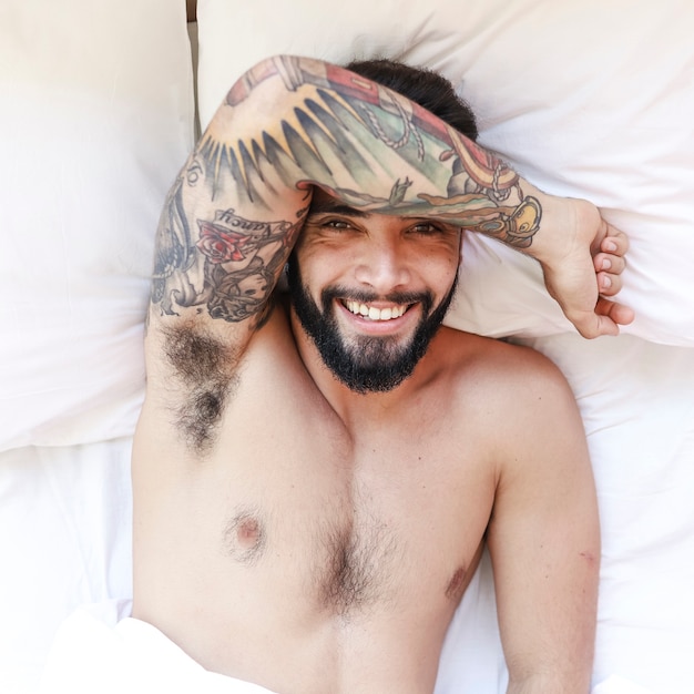 Бесплатное фото Повышенный вид улыбающегося молодого человека, лежащего на кровати