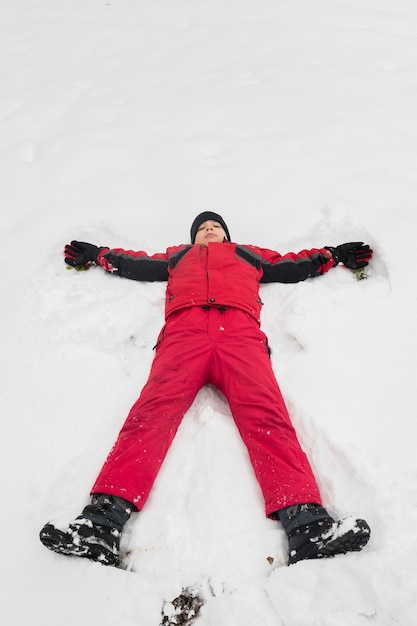 無料写真 白い雪の上に横たわる冬服を持つ少年の立面図