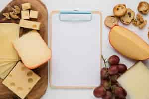 Бесплатное фото Повышенный вид сырного ассорти; грецкий орех; красный виноград и ломтик хлеба с пустой буфер обмена