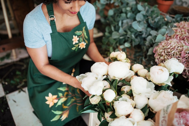 ショップで白い牡丹の花を並べる女性の花屋の上昇したビュー