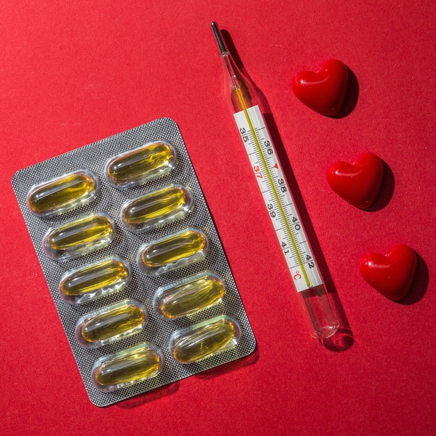 Бесплатное фото Повышенный вид термометра; таблетки и сердца на красном фоне