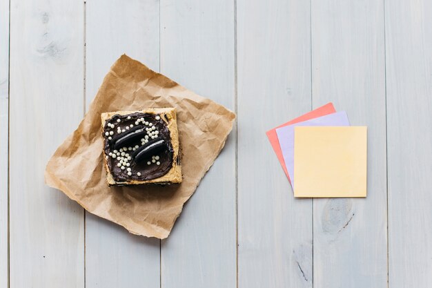 Elevated view of pastry near colorful adhesive notes on wooden background