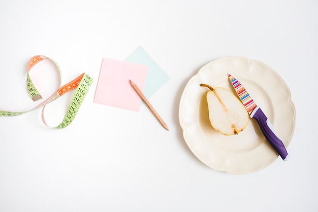 Elevated view of pear on plate near adhesive notes and measuring tape