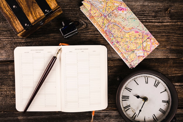 Elevated view of pen, diary, map and clock on wooden background