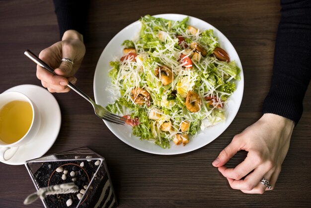 Elevated view of a person having caesar salad with shrimp on white plate over table