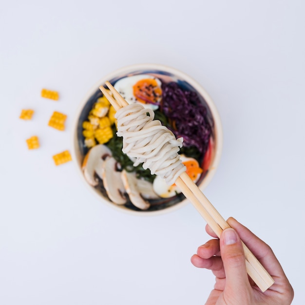 Free photo an elevated view of a person's hand holding noodles on chopsticks over the asian cuisine