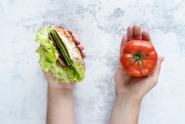 Elevated view of person's hand holding tomato and burger in hand over concrete background