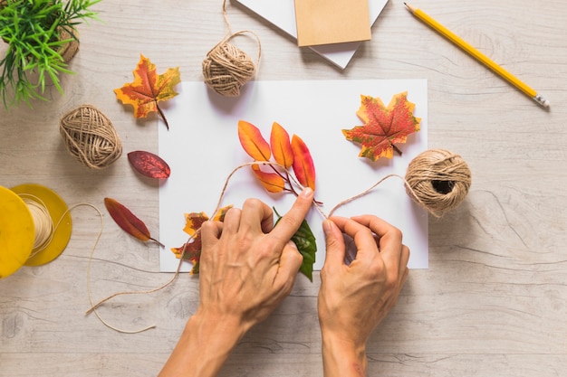 Free photo elevated view of a person tying the fake autumn leaves with string