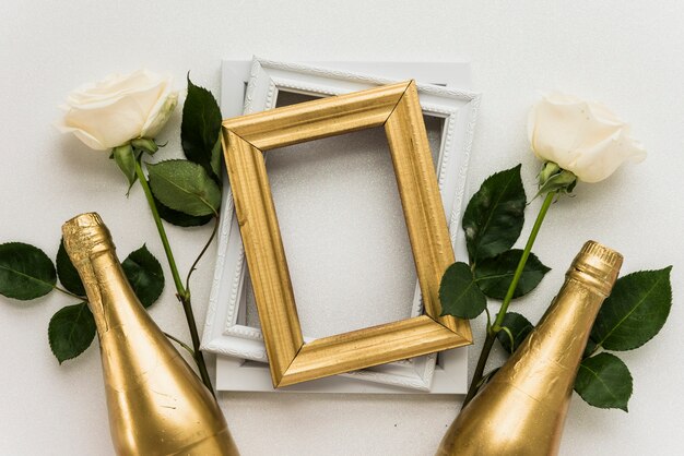 Elevated view of picture frames with two roses and champagne bottle on white surface