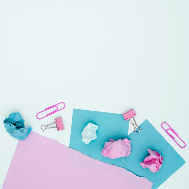 Elevated view of pink and blue card paper and paperclip over white surface