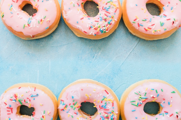 Elevated view of pink donuts in a row on blue background