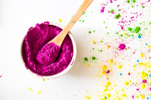 An elevated view of pink holi powder bowl with spoon on white backdrop