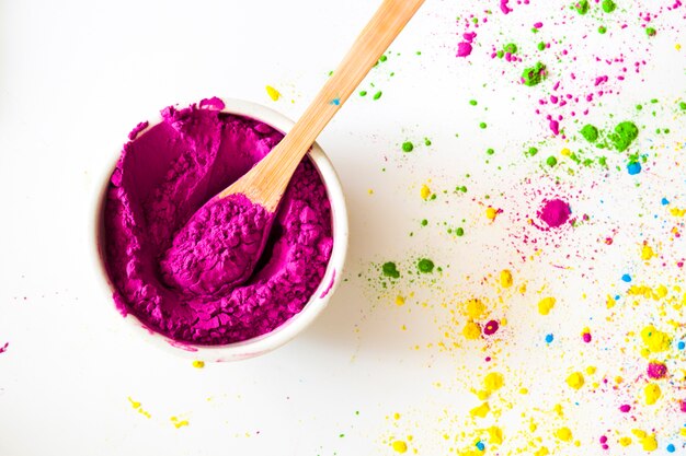 An elevated view of pink holi powder bowl with spoon on white backdrop