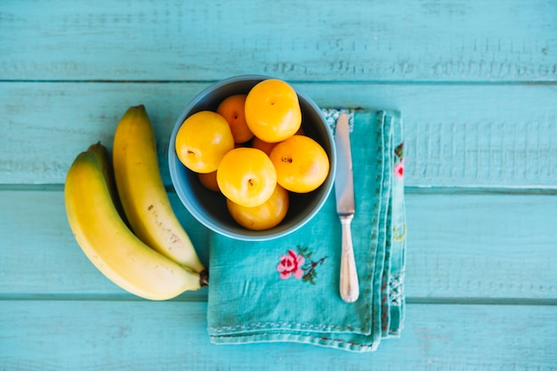 Foto gratuita vista elevata di prugne e banane sullo scrittorio di legno blu