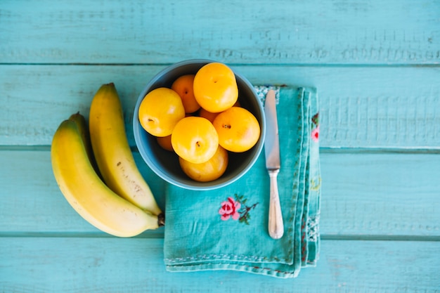 Free photo elevated view of plums and bananas on blue wooden desk