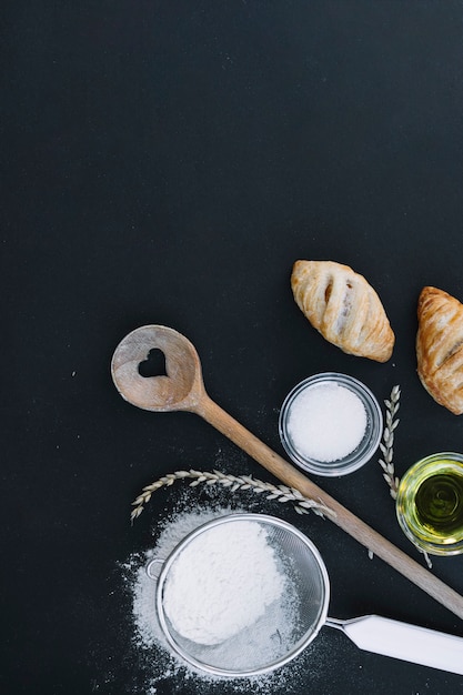 Foto gratuita vista elevata della pasta sfoglia; farina; zucchero; olio; grani e utensili su superficie nera