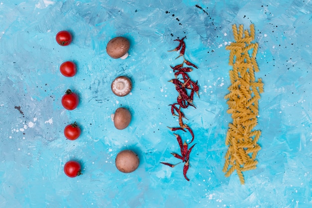 Free photo elevated view of raw pasta and ingredient arranged in row over blue textured surface