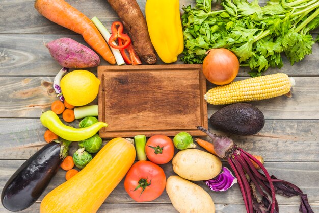 Elevated view of raw vegetables surrounding wooden chopping board