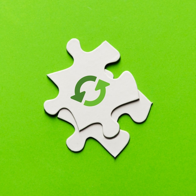 Elevated view of recycling icon on white puzzle piece over green backdrop