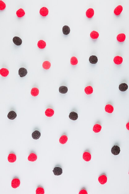 Elevated view of red and black cranberry candies on colored background