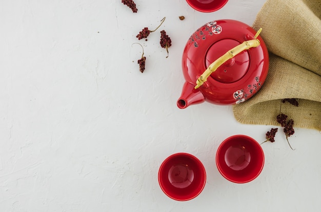 An elevated view of red ceramic teapot and two cups on a black background