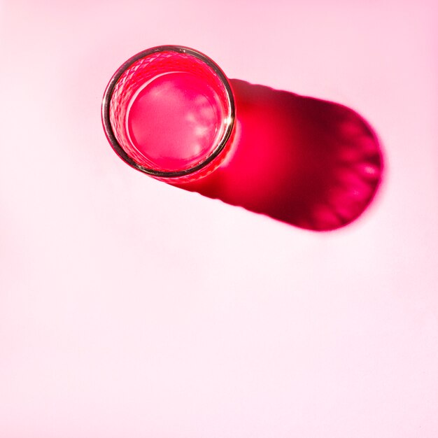 An elevated view of red glass with bright shadow on pink background