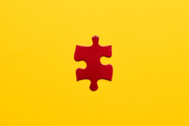 Elevated view of red jigsaw puzzle piece on yellow backdrop