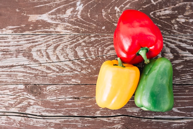 An elevated view of red; yellow and green bell peppers on an old wooden desk