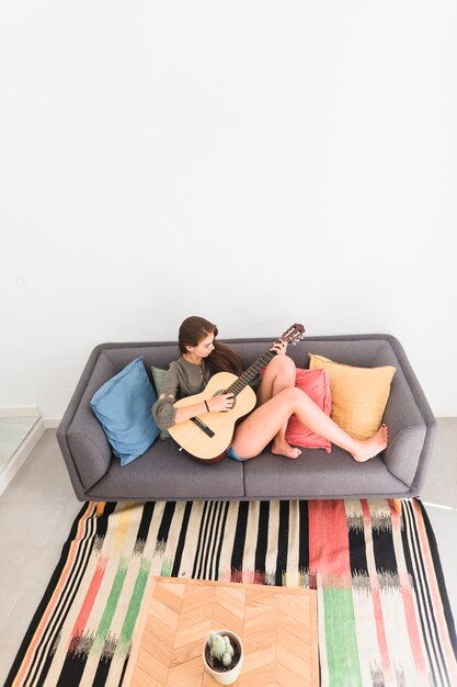 Elevated view of relaxed teenage girl sitting on sofa playing guitar