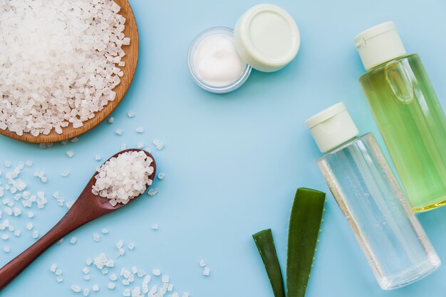 An elevated view of rock salts; cream and aloevera spray bottles on blue background