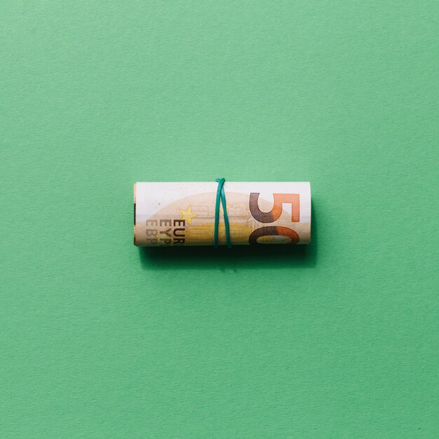 Elevated view of rolled up fifty euro note on green background