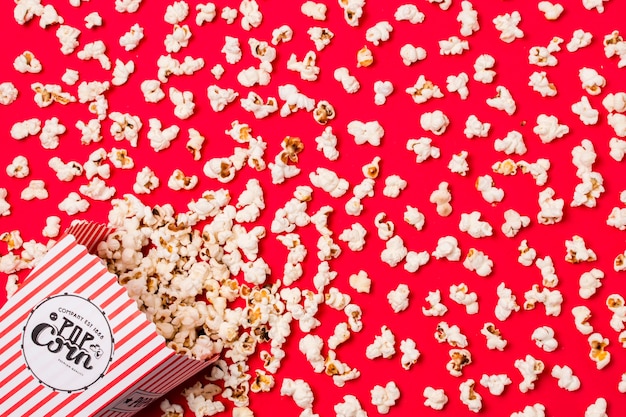 An elevated view of salty spilled popcorns from box on red backdrop