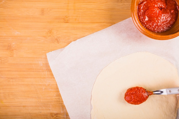 Elevated view of sauce and dough on wooden table