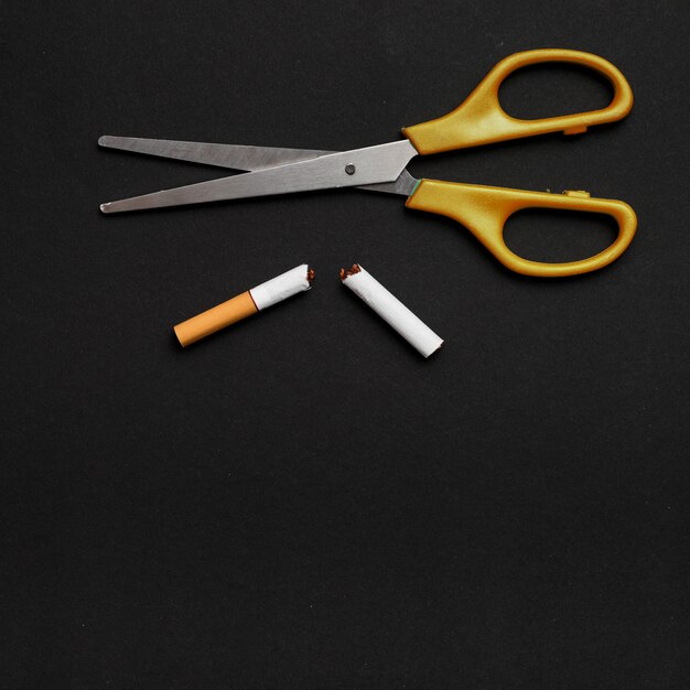 Elevated view of scissor and broken cigarette over black background