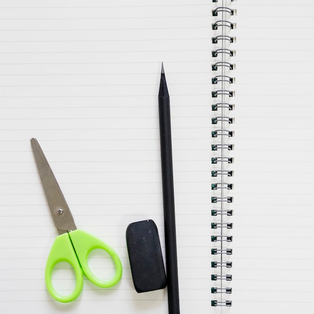 Elevated view of scissors; eraser and pencil on spiral notebook