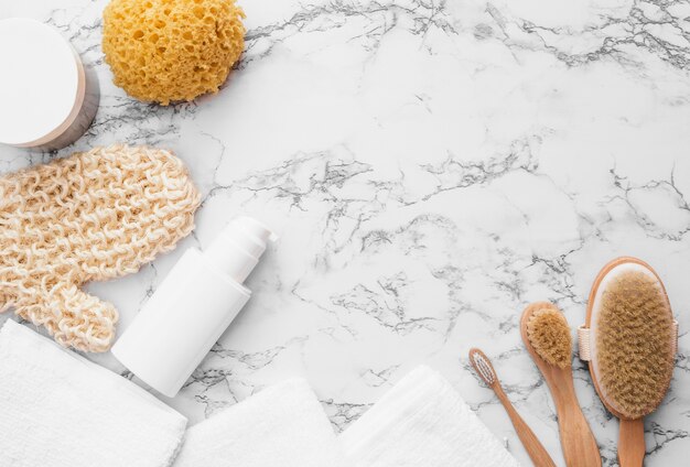 Elevated view of scrub glove; sponge; brush; towel and moisturizing cream on marble background