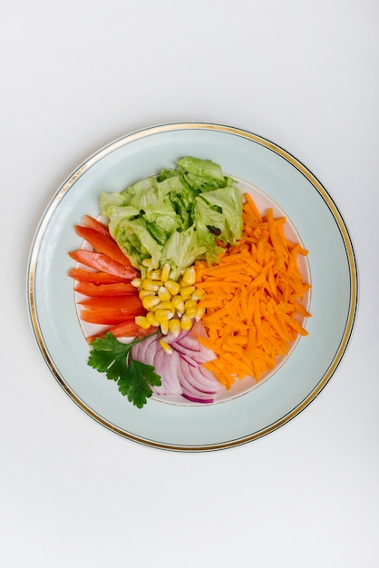 Elevated view of sliced carrot; lettuce; tomato; corn; onion and parley on plate