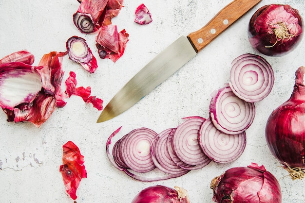 Elevated view of sliced onion; knife and peels over concrete background