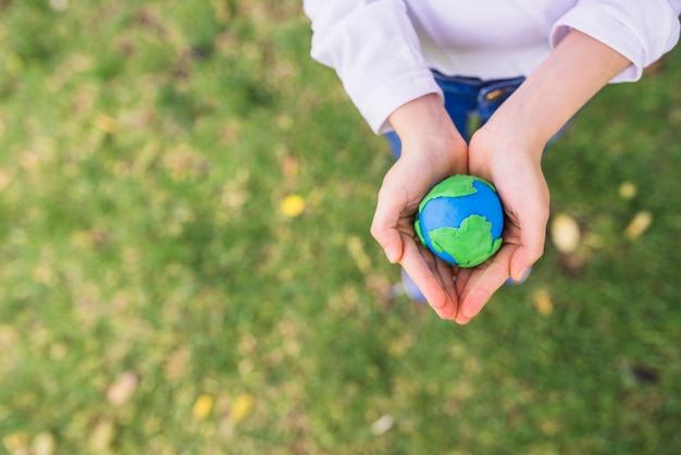 Free photo elevated view of small clay globe in cupped hands over grass