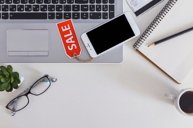 Elevated view of smartphone with sale tag on laptop keypad over the white table