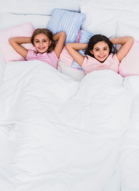 An elevated view of smiling girls lying on bed looking to camera