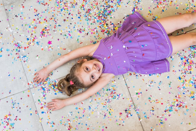 Elevated view of smiling little girl lying on floor with confetti