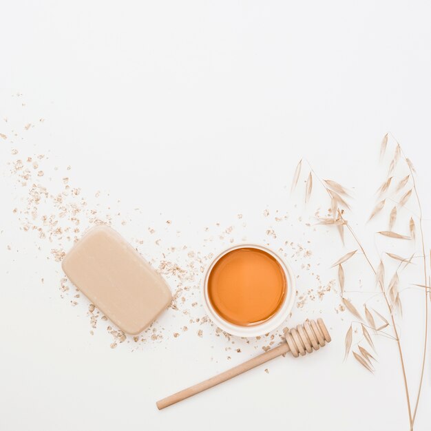 Elevated view of soap; honey; honey dipper and hush on white surface