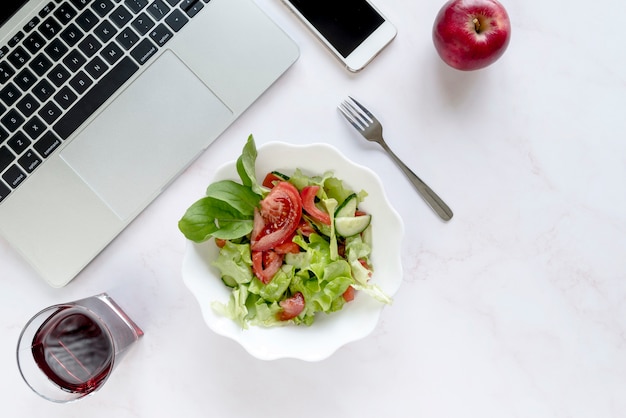 Free photo elevated view of soft drink; bowl of salad; apple and fork near electronic devices over white background