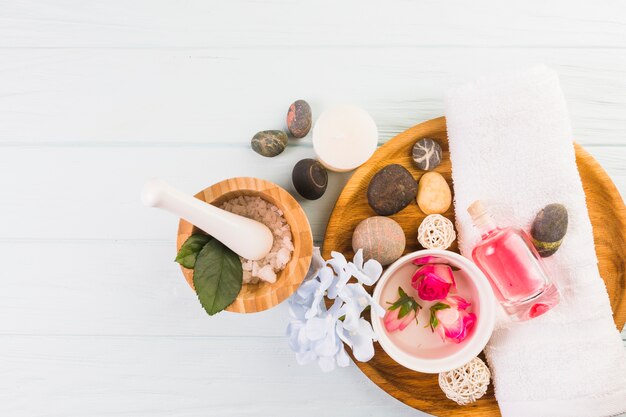 Elevated view of spa stones; salt; towel; flowers and oil on white background