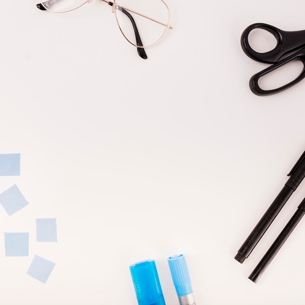 Elevated view of spectacles; pen; scissors and adhesive notes on white background