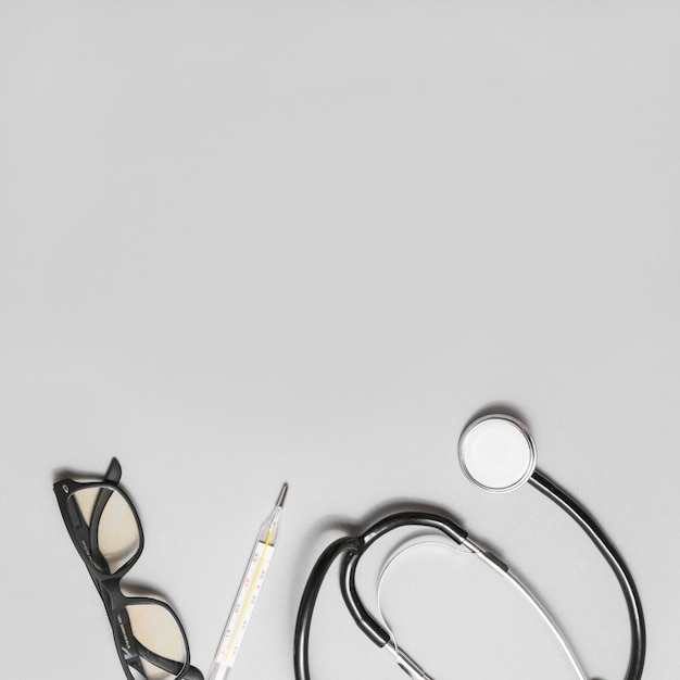 Elevated view of spectacles; stethoscope and thermometer on grey background